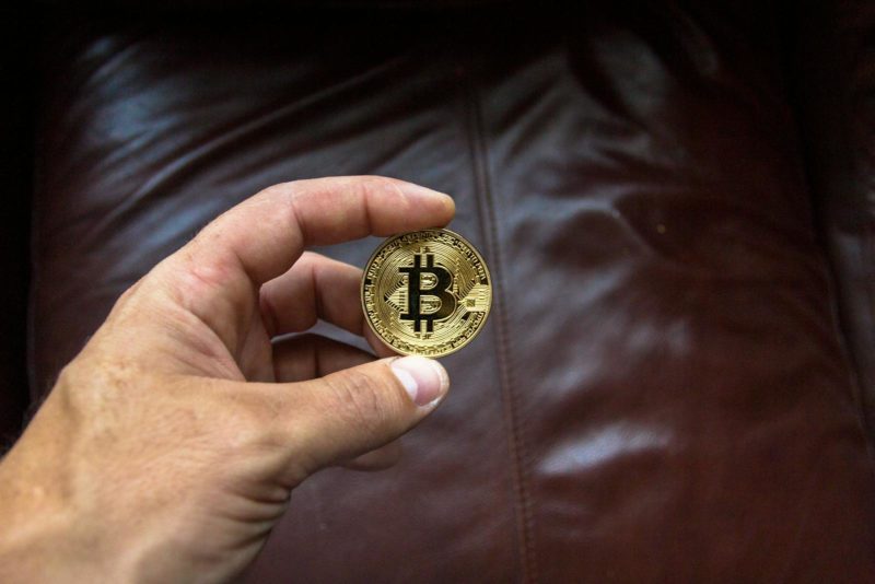 Close-up of a hand holding a gold Bitcoin cryptocurrency coin on a leather background.