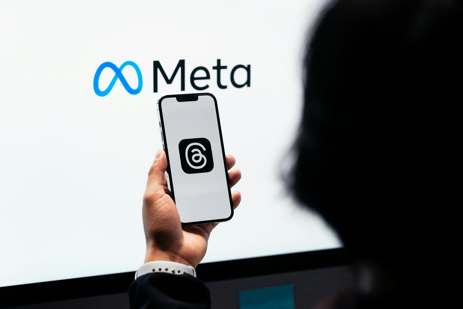 Hands holding smartphone with Meta Threads logo on screen, Meta branding in background.