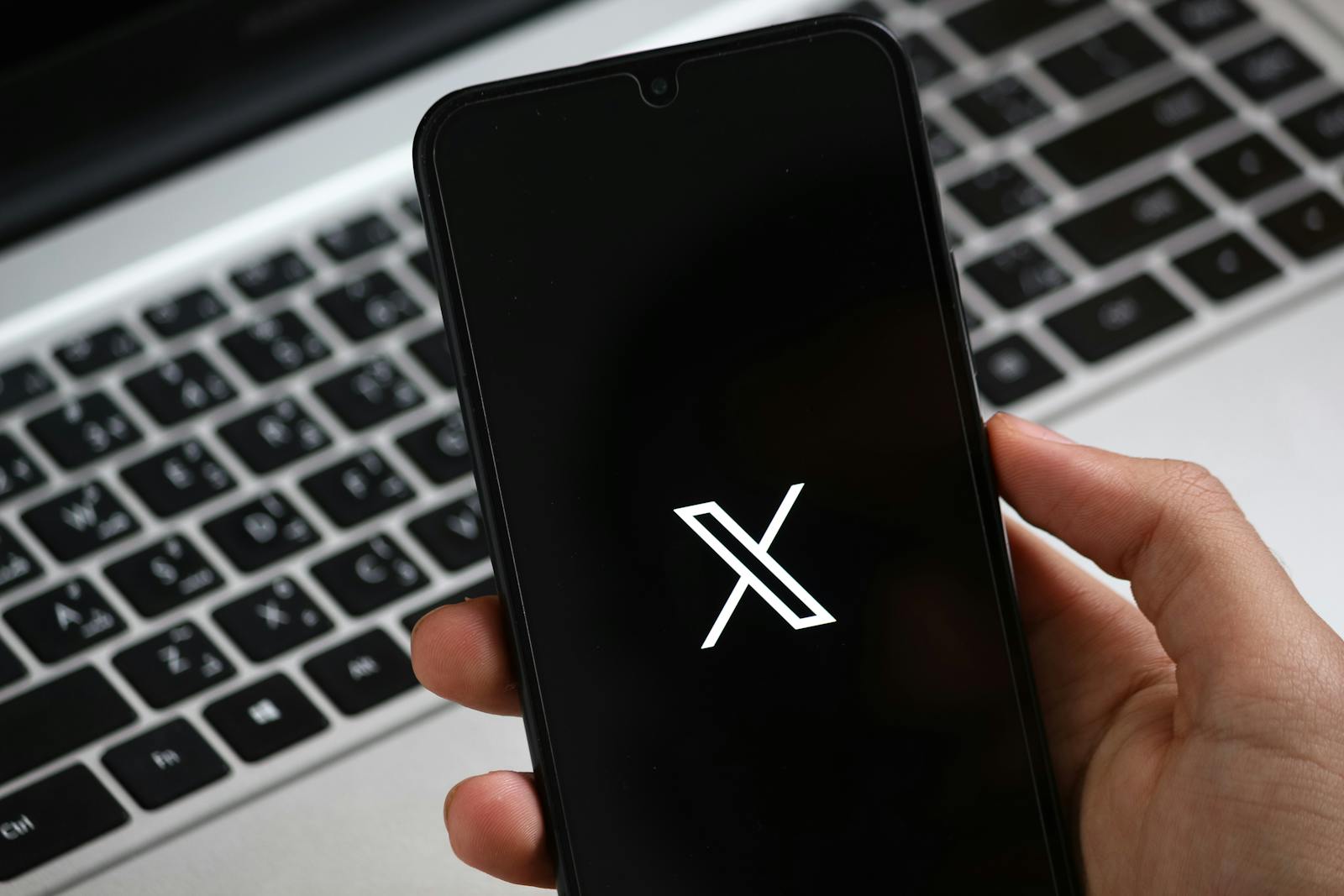 A hand holds a smartphone displaying a modern app interface, with a laptop keyboard in the background.